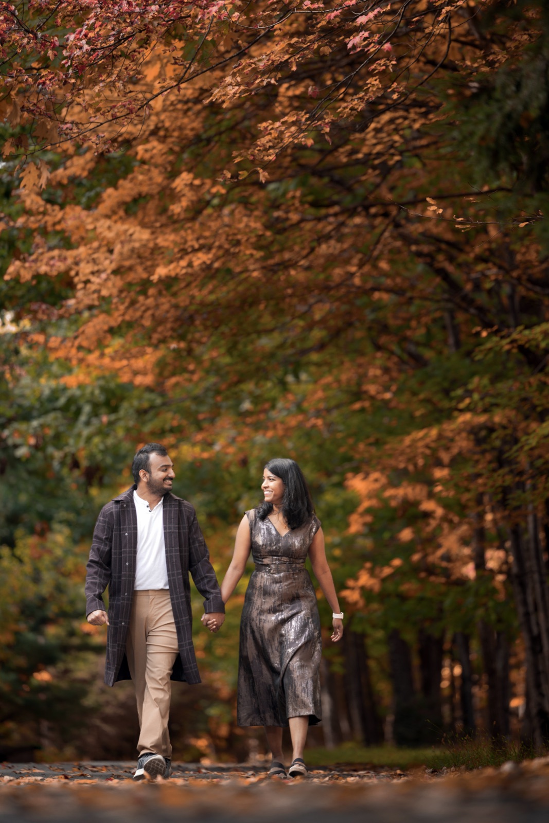 Dheekshitha and Siddharth walking hand in hand beneath golden autumn trees