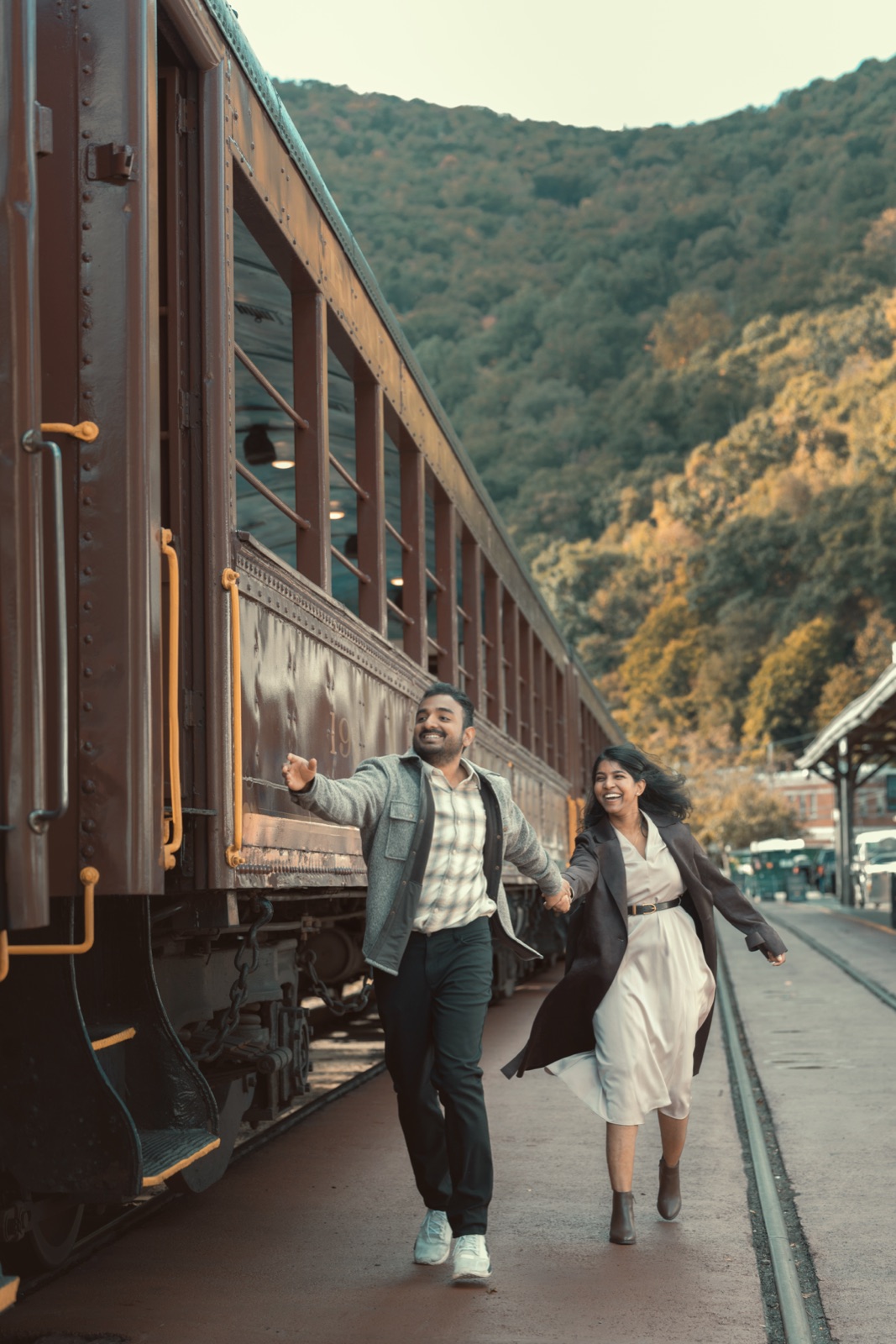Dheekshitha and Siddharth laughing and holding hands beside a vintage train